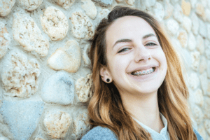 Smiling young woman wearing metal braces beside a stone wall