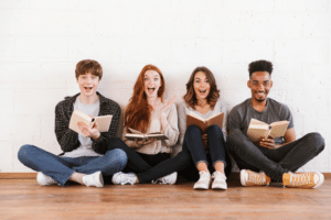 Four smiling college students sitting together and holding open books.